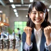 A joyful scene of a Japanese professional feeling happy and successful after securing a new job at a company specializing in spark plugs and ceramics products. The setting is a bright, modern office with hints of industrial design. The person is smiling and looking confident, with a positive atmosphere surrounding the workplace.